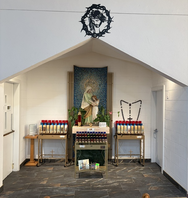 A devotional prayer nook with a statue of Saint Anne and the Virgin Mary, votive candles, and a rosary display.